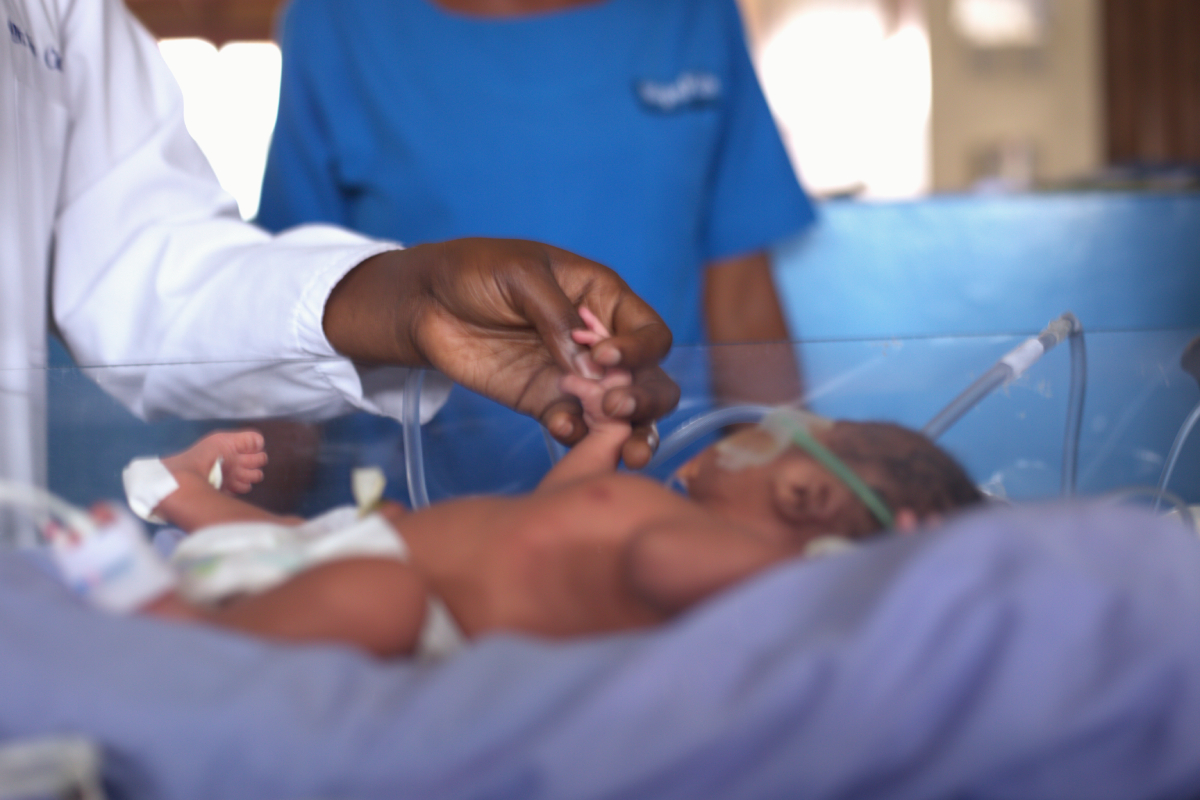 Photo of a newborn infant holding the hand of a doctor.