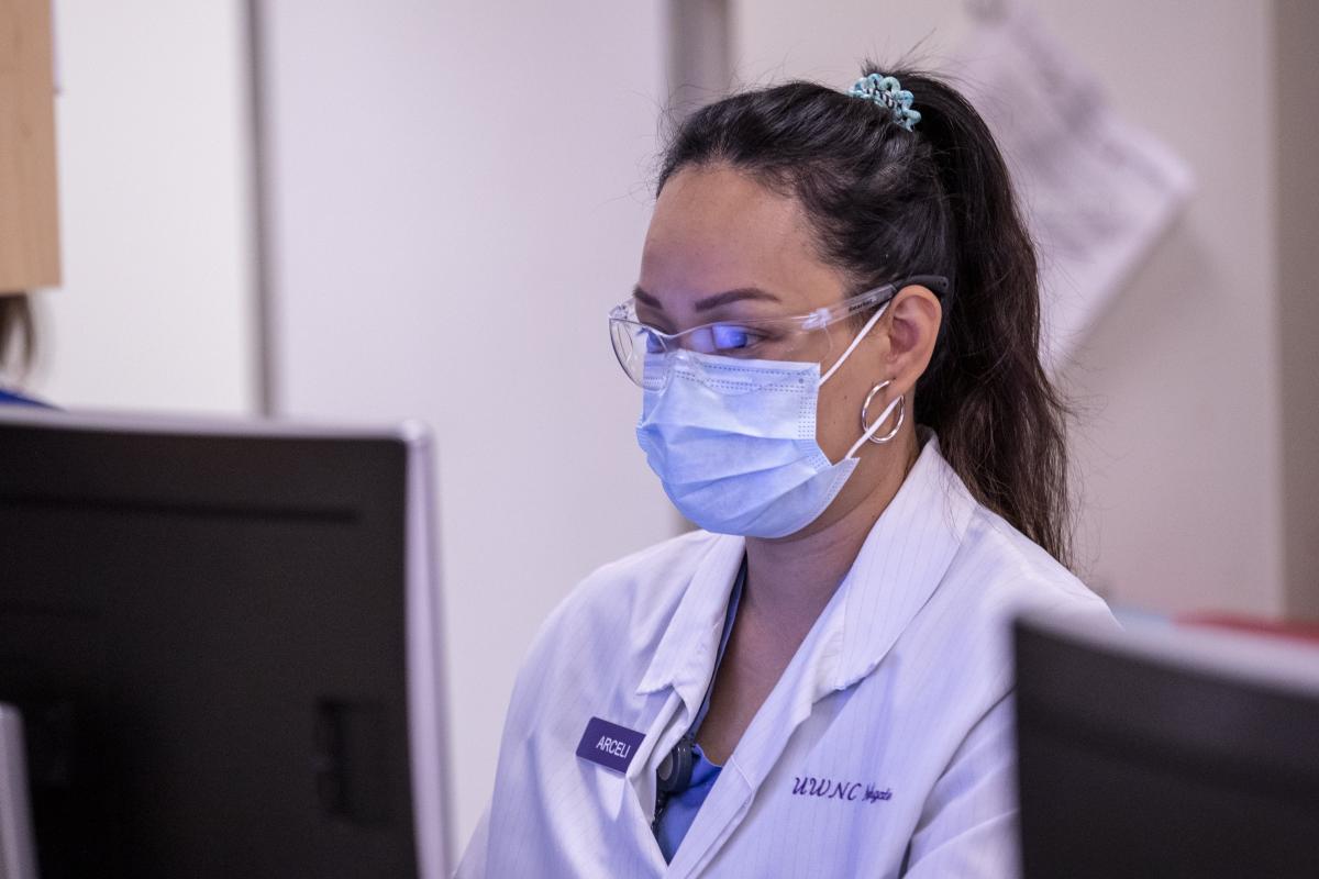 Photo of a masked medical worker sitting at a computer.